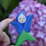 An Ostheimer hand made and hand painted wooden Gentian Flower Child figure toy held in an adult's hand to show scale. These flower child wooden figures are part of a wide range of expertly hand crafted wooden toys here at Babipur. 