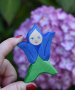 An Ostheimer hand made and hand painted wooden Gentian Flower Child figure toy held in an adult's hand to show scale. These flower child wooden figures are part of a wide range of expertly hand crafted wooden toys here at Babipur. 