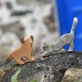 Ostheimer German shepherd wooden toy figure with a striped grey jumping cat placed on a stone wall outdoors. 