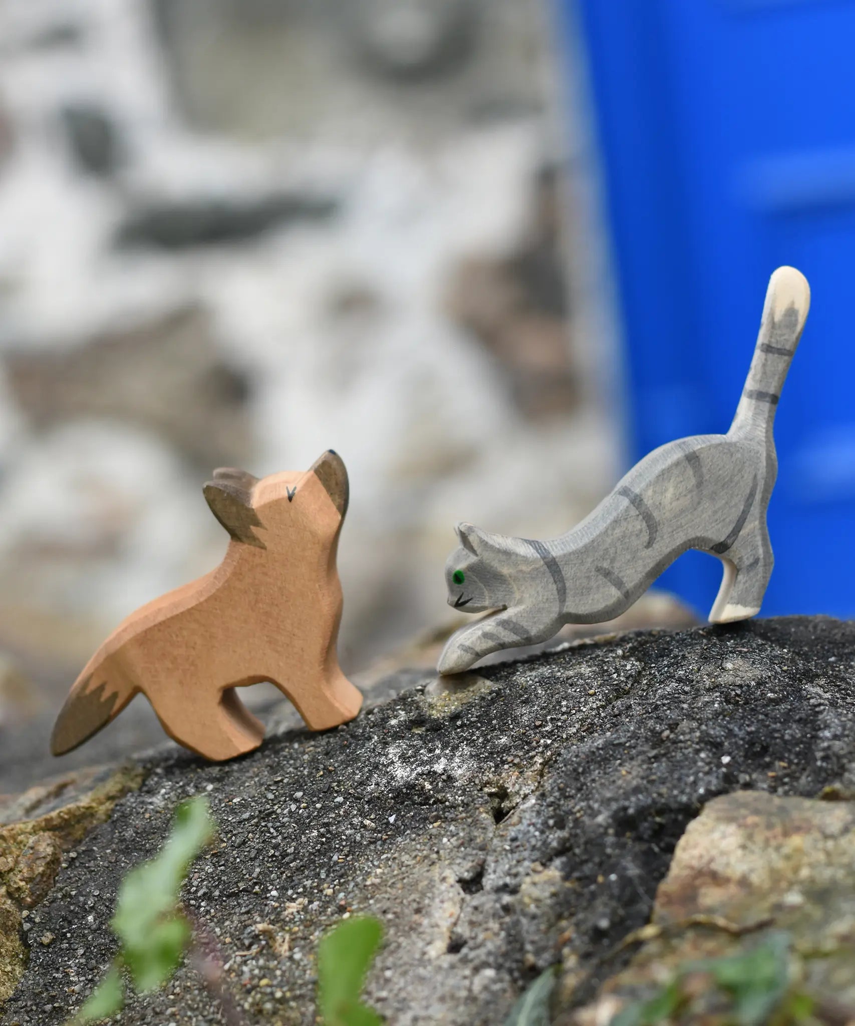 Ostheimer German shepherd wooden toy figure with a striped grey jumping cat placed on a stone wall outdoors. 