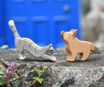 Ostheimer German shepherd wooden toy figure with a striped grey jumping cat placed on a stone wall outdoors. 