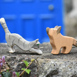 Ostheimer German shepherd wooden toy figure with a striped grey jumping cat placed on a stone wall outdoors. 