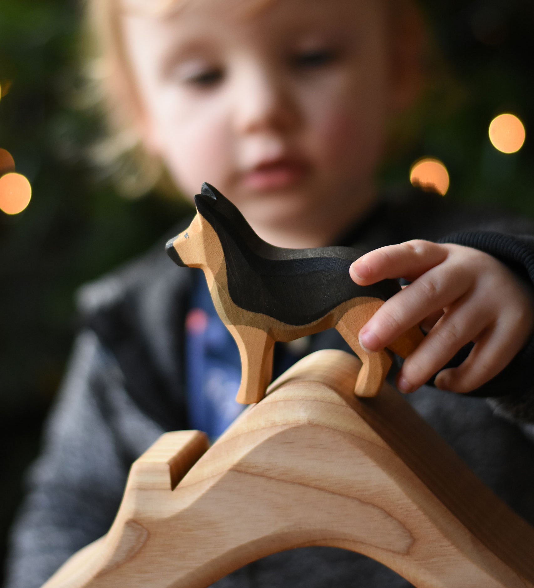 A child playing with an Ostheimer German shepherd dog wooden toy figure, placing it on the roof of a house shaped wooden piece. These wooden figures are part of a wide range of expertly hand crafted wooden toys here at Babipur. 