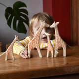 Ostheimer giraffe family placed on a wooden surface in front of a child.  Running standing, small with head low and small with head high giraffes. 