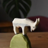White Ostheimer wooden goat figure placed on top of a medium green bush piece. 