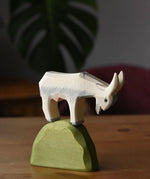 White Ostheimer wooden goat figure placed on top of a medium green bush piece. 
