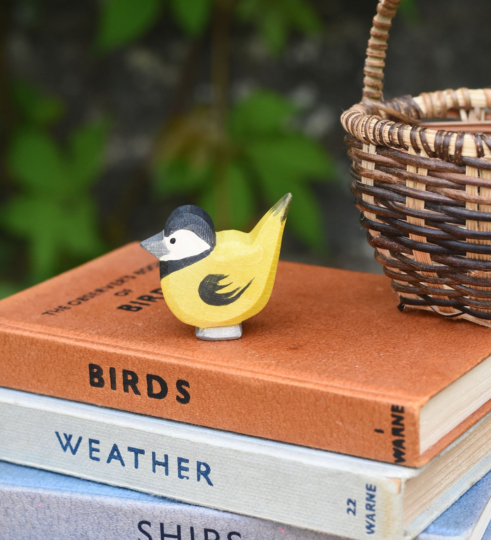 An Ostheimer bird figure placed on top of a pile of old books next t a Kraul basket.