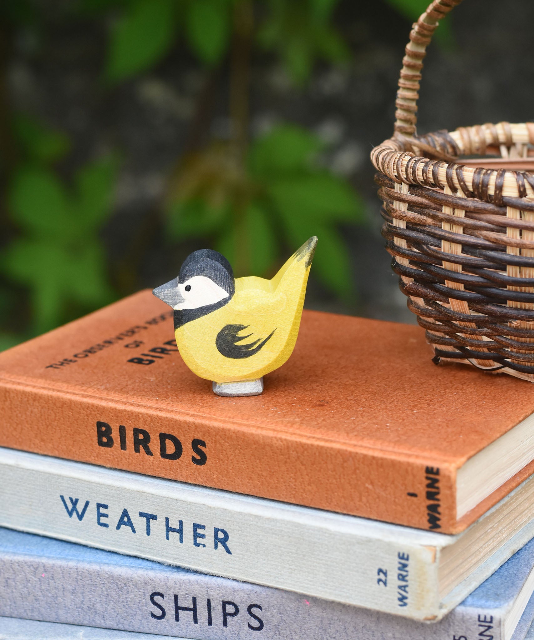 An Ostheimer bird figure placed on top of a pile of old books next t a Kraul basket.