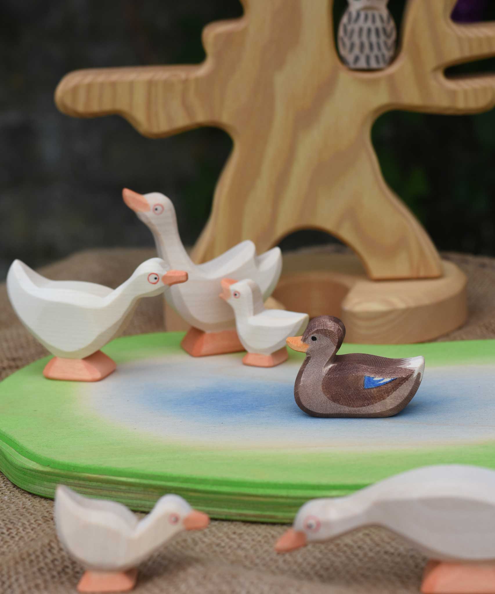 A gaggle of Ostheimer woodengeese and goslings on a wooden pond scene piece with the bird tree with an owl on the branch on the background.