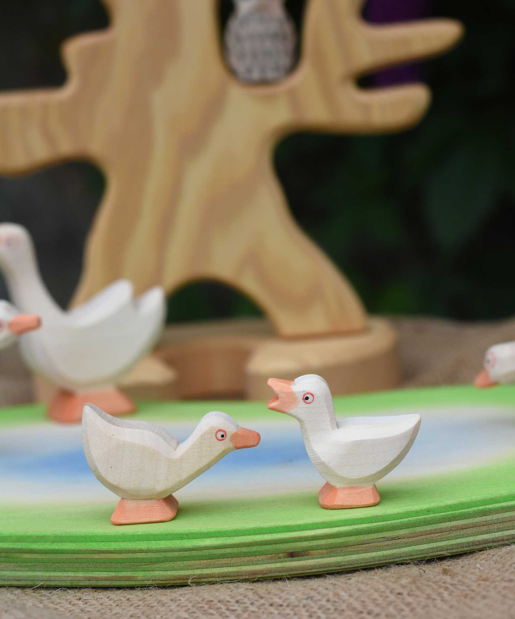 Two Ostheimer goslings placed on a wooden pond scene piece. one goslings has it's head held high and the other has it's head low.
