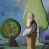 An Ostheimer grandfather wooden toy figure placed in the middle of a small world play scene. There are Ostheimer trees in the background. This wooden figure is part of a large range of expertly hand crafted, Waldorf inspired, wooden toys here at Babipur. 