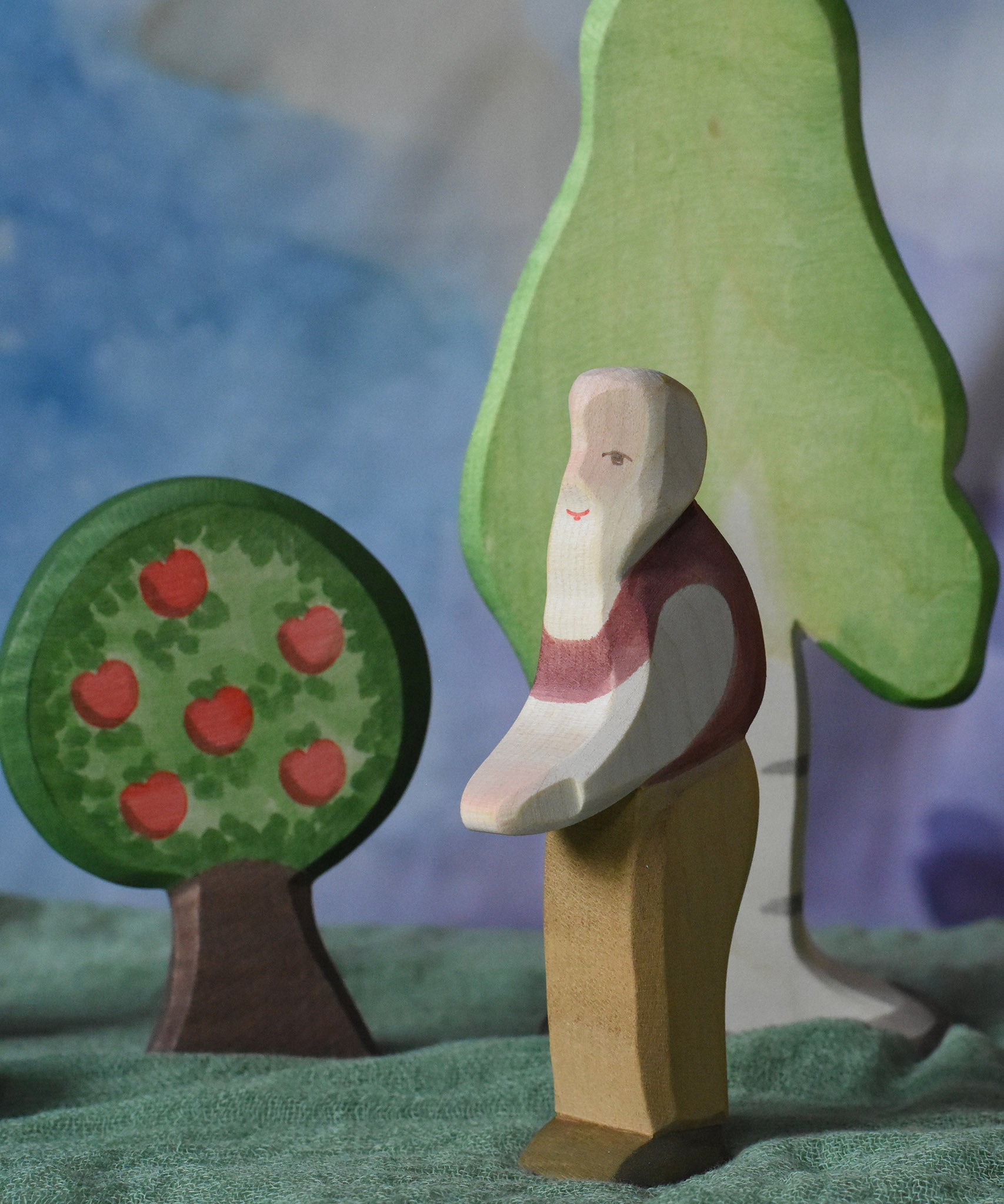 An Ostheimer grandfather wooden toy figure placed in the middle of a small world play scene. There are Ostheimer trees in the background. This wooden figure is part of a large range of expertly hand crafted, Waldorf inspired, wooden toys here at Babipur. 