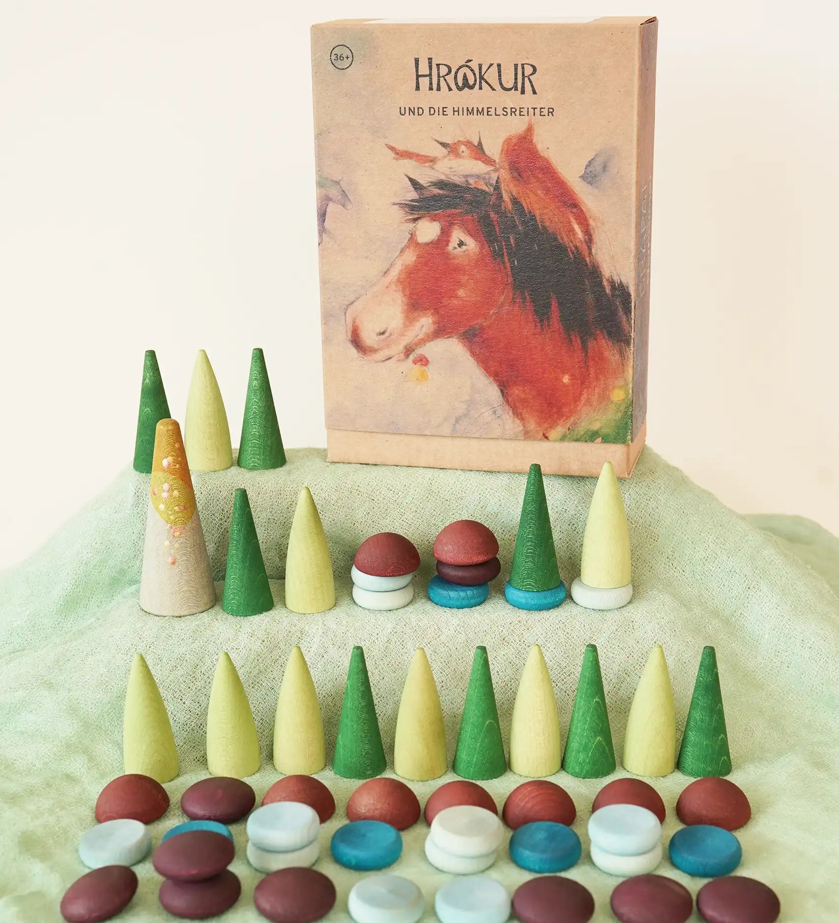 Grapat x Ostheimer Hrókur Mandala Pieces Set Wooden Toy placed on green Ostheimer cotton scarf. The box featuring an illustration of the brown horse is placed next to them in the Babipur playroom.