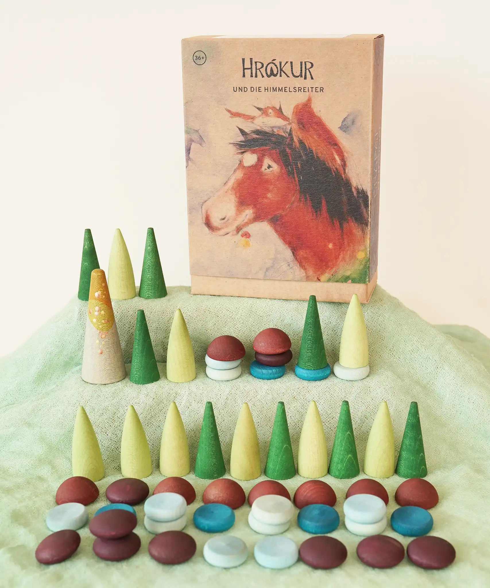 Grapat x Ostheimer Hrókur Mandala Pieces Set Wooden Toy placed on green Ostheimer cotton scarf. The box featuring an illustration of the brown horse is placed next to them in the Babipur playroom.