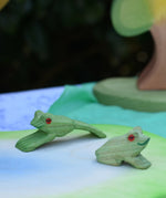 Ostheimer jumping and sitting frogs  handmade wooden toy figures placed on a pond scenery play piece. 