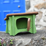 Ostheimer green hutch for toy animals with it's door opened placed on a stone wall outdoors.