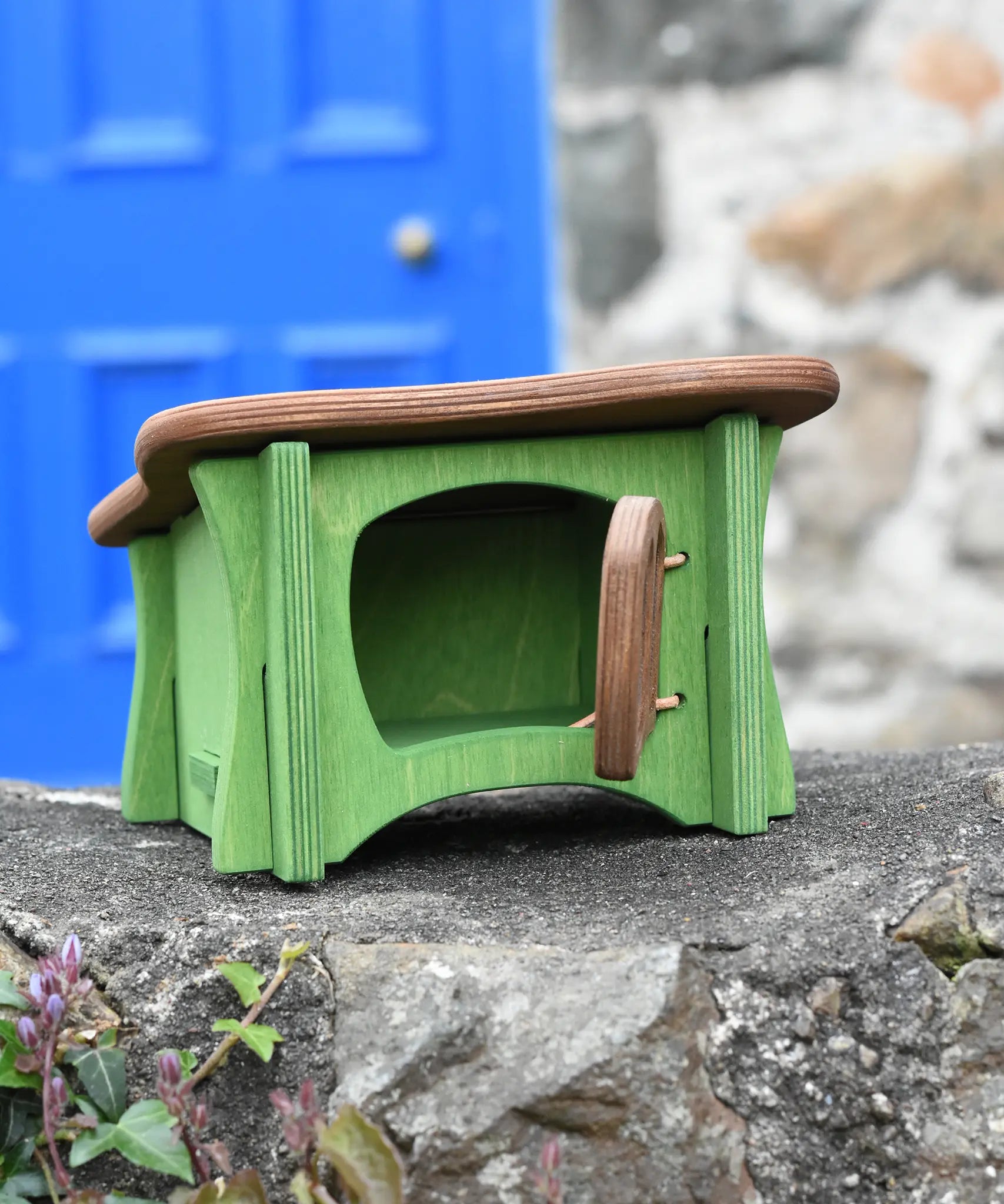 Ostheimer green hutch for toy animals with it's door opened placed on a stone wall outdoors.