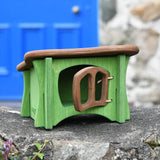 Ostheimer green hutch for toy animals with it's brown door open placed on a stone wall outside.