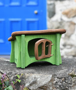 Ostheimer green hutch for toy animals with it's brown door open placed on a stone wall outside.
