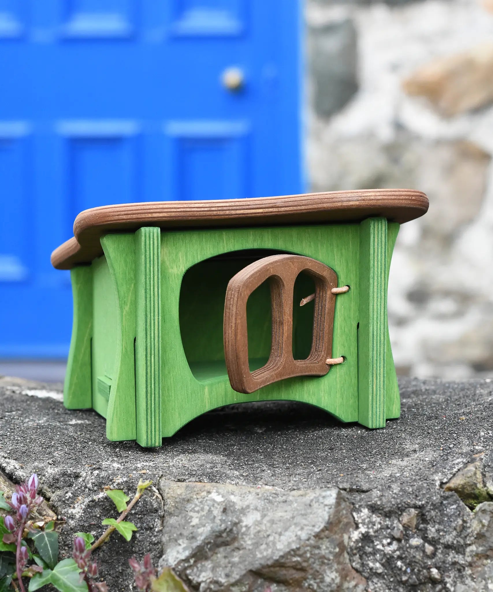Ostheimer green hutch for toy animals with it's brown door open placed on a stone wall outside.