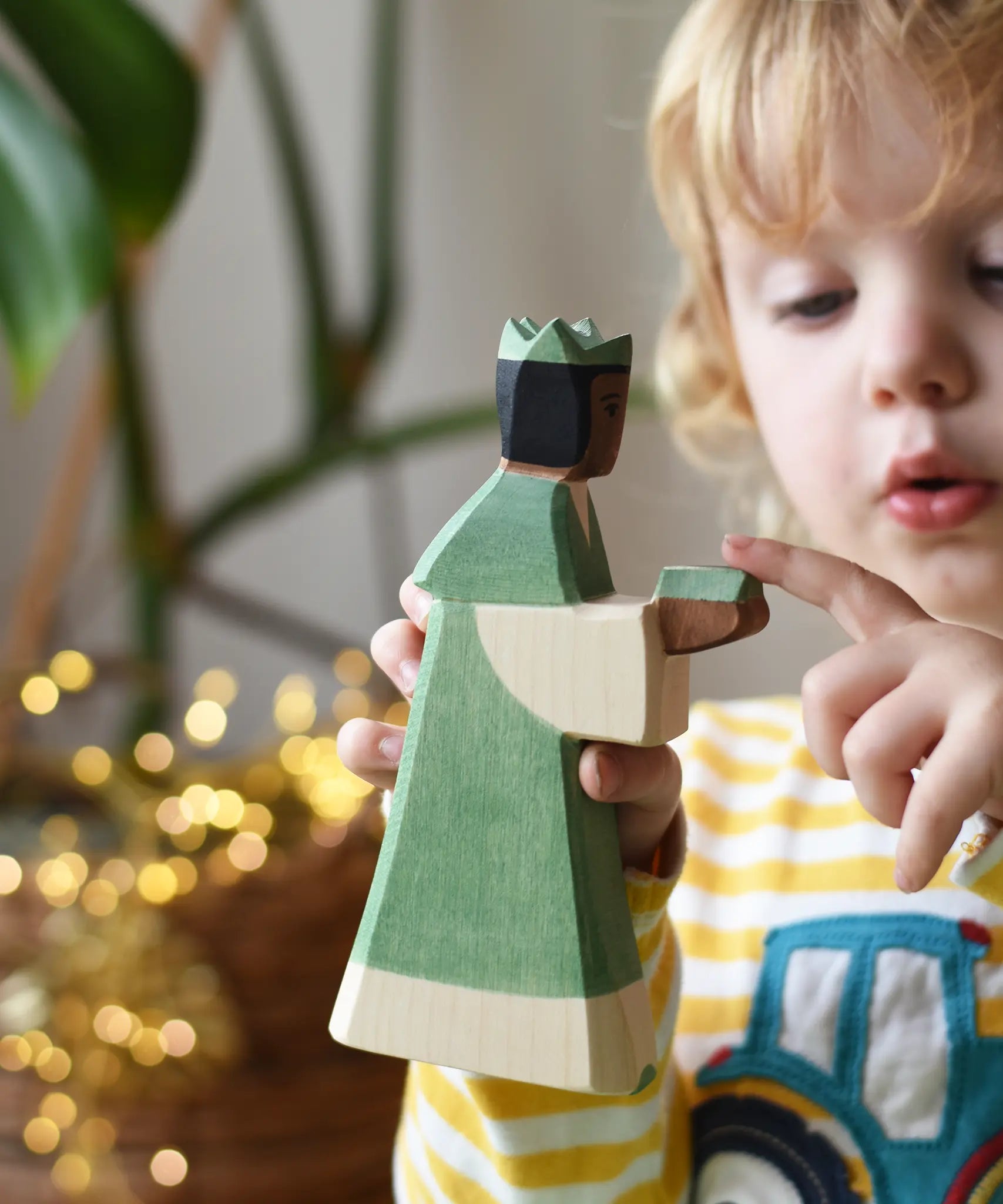 Ostheimer green king wooden toy figure in a child's hand. Child pointing at the gift in the figure's hands.