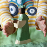 Ostheimer green king wooden toy figure placed on a cotton green play cloth with a child's hand going in to hold it. 