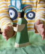 Ostheimer green king wooden toy figure placed on a cotton green play cloth with a child's hand going in to hold it. 
