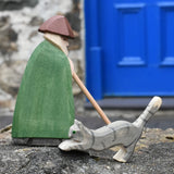 Ostheimer grey striped jumping car wooden toy figure placed on a stone wall with a shepherd behind it on a stone wall outdoors.