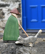 Ostheimer grey striped jumping car wooden toy figure placed on a stone wall with a shepherd behind it on a stone wall outdoors.