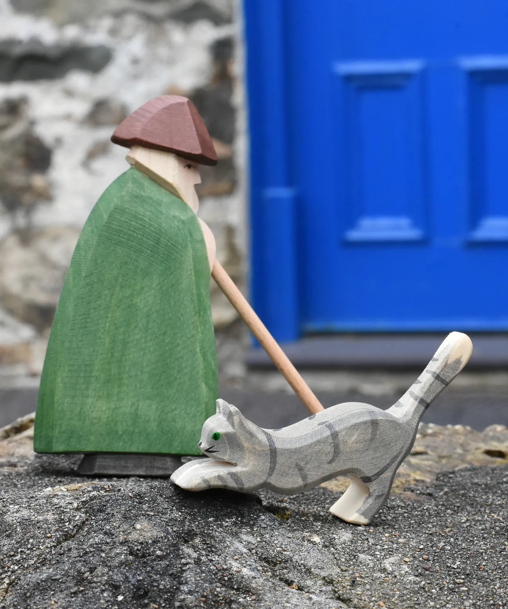 Ostheimer grey striped jumping car wooden toy figure placed on a stone wall with a shepherd behind it on a stone wall outdoors.