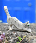 Ostheimer grey striped jumping car wooden toy figure placed on a stone wall outdoors.