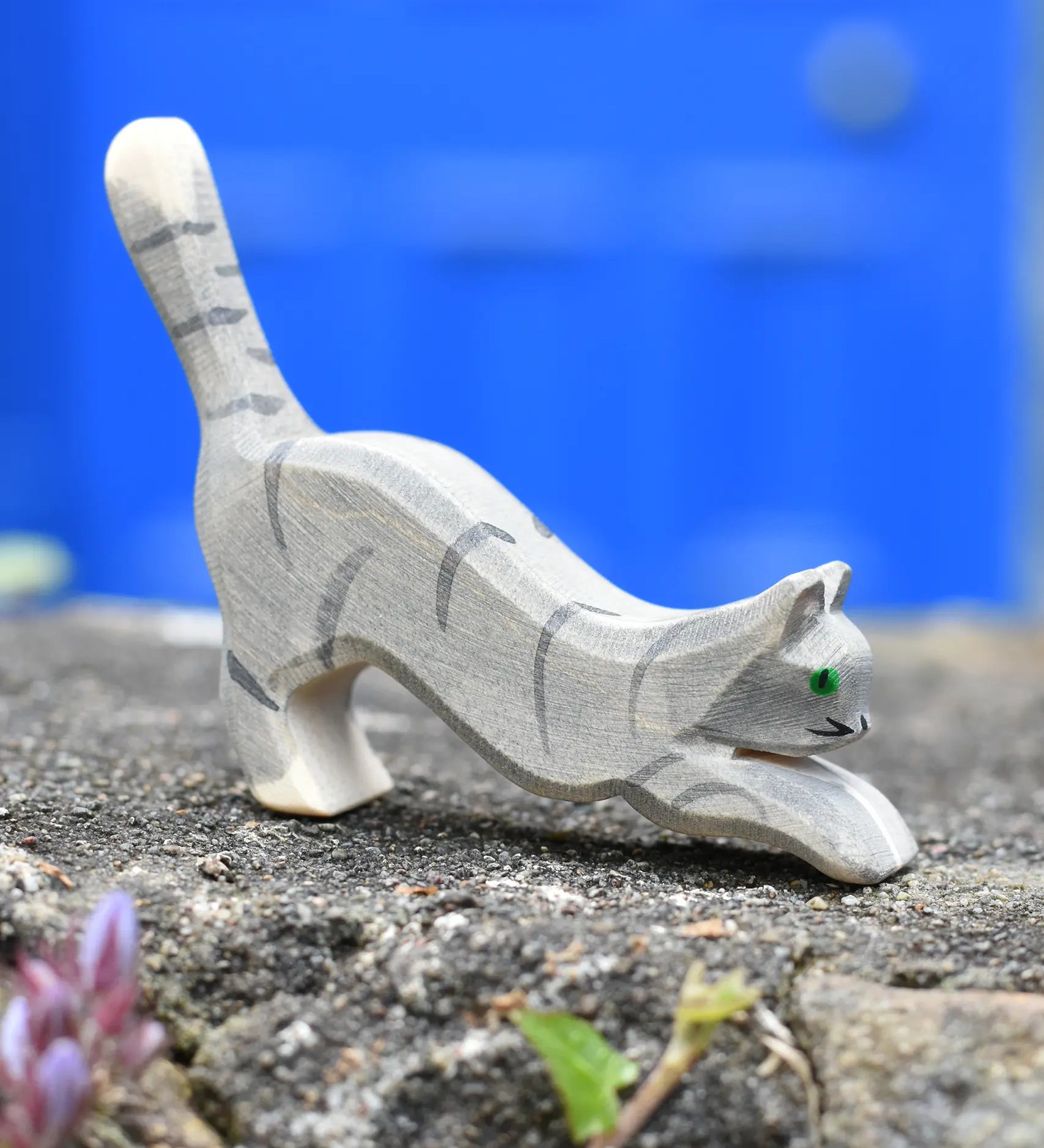 Ostheimer grey striped jumping car wooden toy figure placed on a stone wall outdoors.