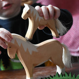 Child placing an Ostheimer haflinger colt wooden toy figure on top of a haflinger horse figure.