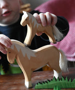 Child placing an Ostheimer haflinger colt wooden toy figure on top of a haflinger horse figure.