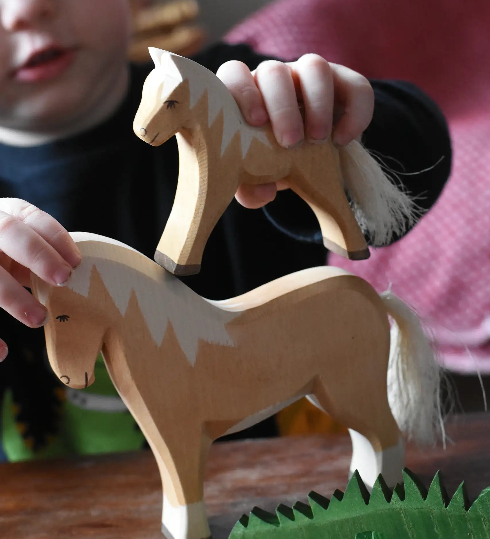 Child placing an Ostheimer haflinger colt wooden toy figure on top of a haflinger horse figure.