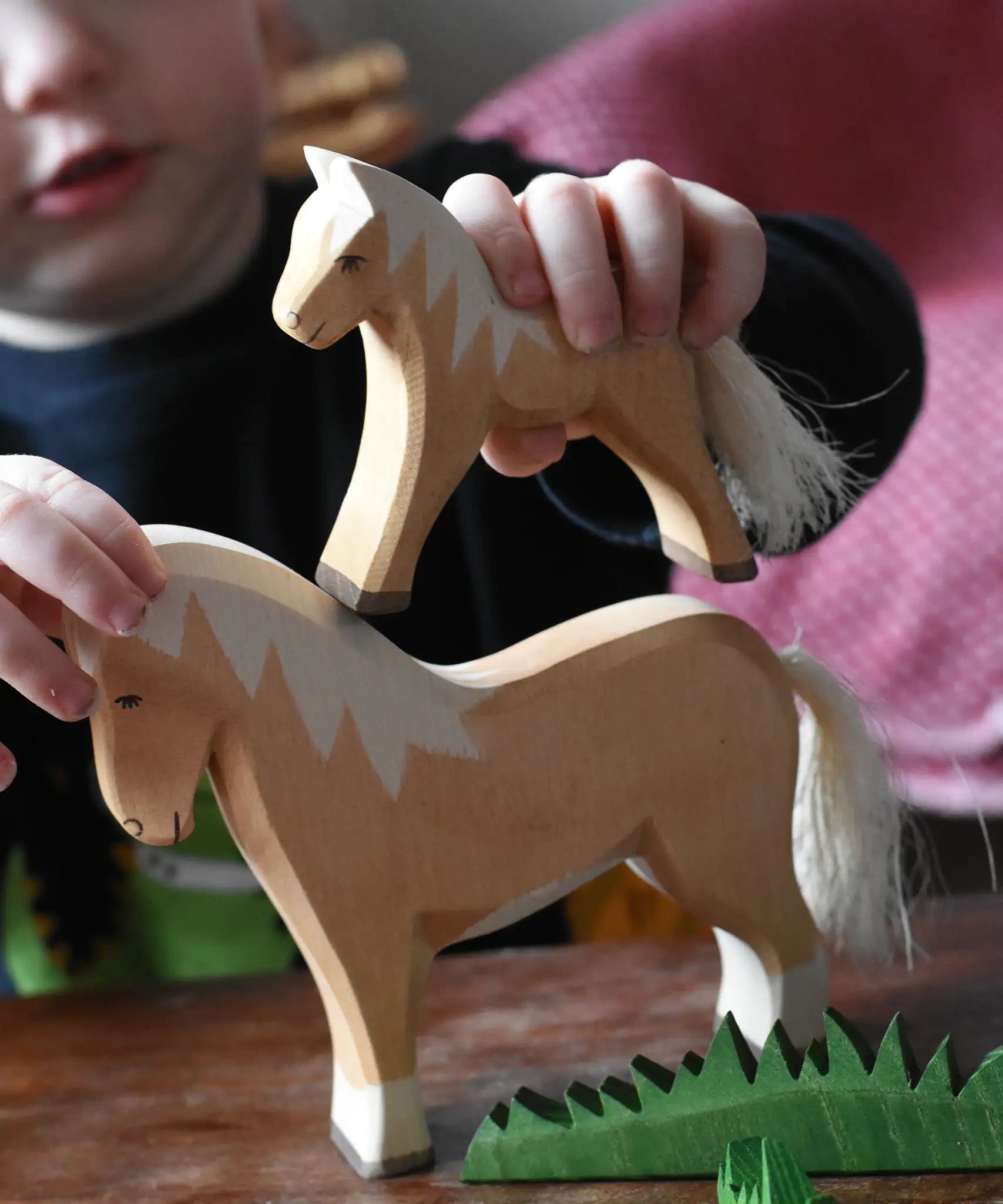 Child placing an Ostheimer haflinger colt wooden toy figure on top of a haflinger horse figure.