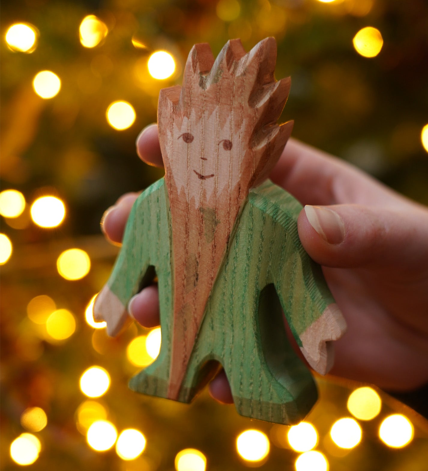 The wooden Tree Troll toy figure by Ostheimer, a hand carved and hand painted imaginative play toy held in front of a Christmas Tree.