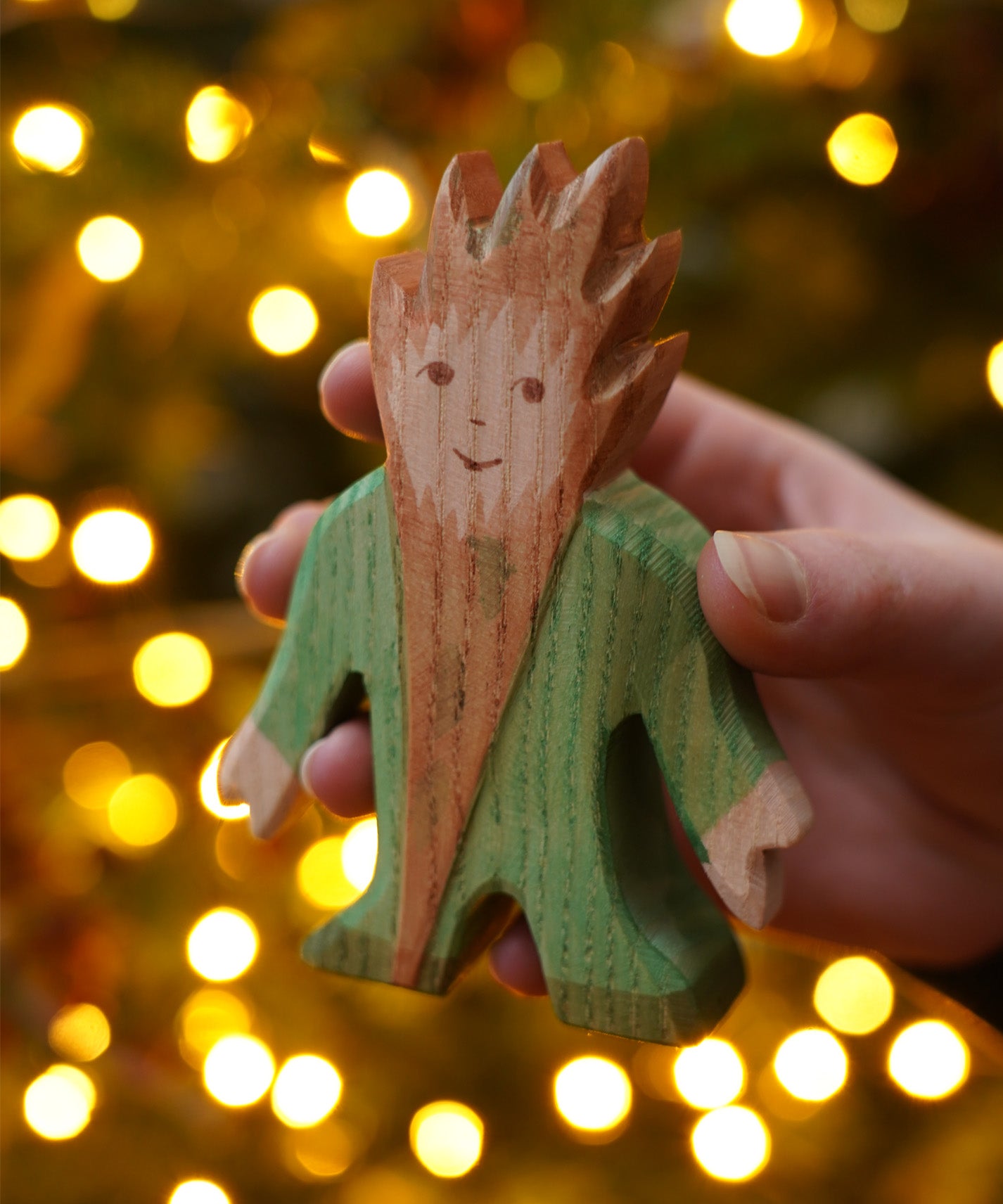 The wooden Tree Troll toy figure by Ostheimer, a hand carved and hand painted imaginative play toy held in front of a Christmas Tree.