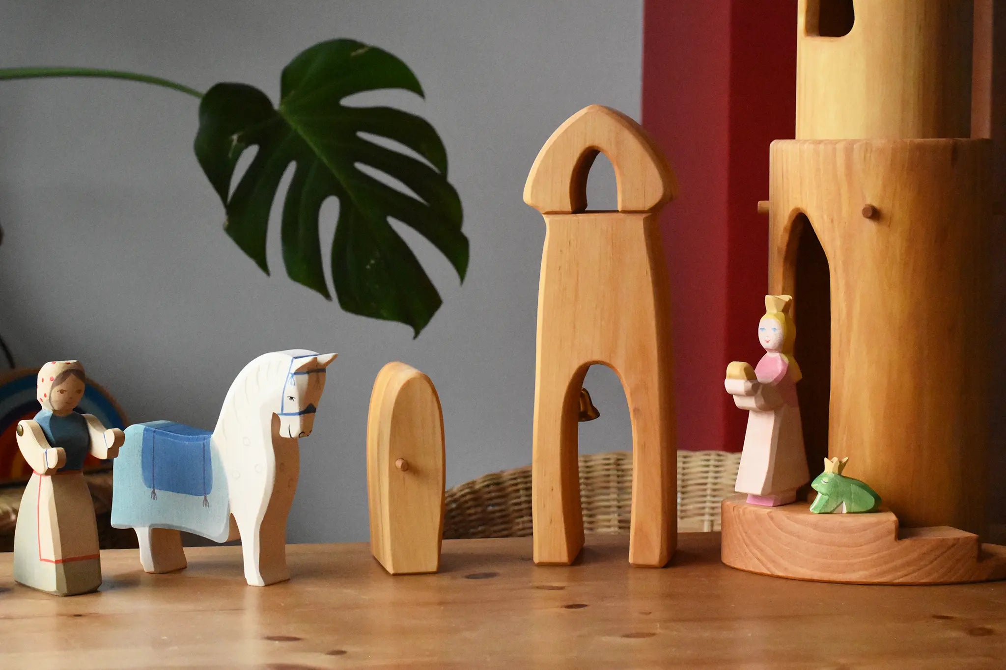 Small world play scene featuring a selection of Ostheimer handmade wooden toys and figures. Female farmer, horse with blue saddle, sentry post with bell, princess, frog king and castle round tower with stairs.
