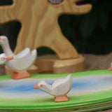 An Ostheimer gosling with it's head low placed on a pond scene piece. Other Ostheimer geese and a wooden bird tree can be seen in the background.