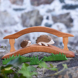 Two wooden Ostheimer hedgehog figures placed on a wooden toy bridge in a small world play scene. Wooden grass can be seen in the foreground. Check out our full range of expertly crafted wooden toy figures and scenery here at Babipur.