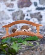 Two wooden Ostheimer hedgehog figures placed on a wooden toy bridge in a small world play scene. Wooden grass can be seen in the foreground. Check out our full range of expertly crafted wooden toy figures and scenery here at Babipur.