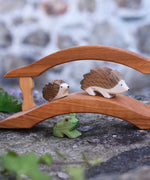 Ostheimer hedgehogs, large and small placed on a wooden bridge with a green frog underneath. Check out our full range of expertly crafted wooden toy figures and scenery here at Babipur.