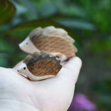A small wooden Ostheimer hedgehog shown on an adult's hand for scale, with a large hedgehog in the background. 