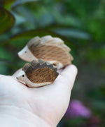 A small wooden Ostheimer hedgehog shown on an adult's hand for scale, with a large hedgehog in the background. 