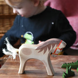 Ostheimer wooden white horse for rider toy figure placed at the front of a small world play scene with green grass scenery pieces. 