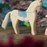 An Ostheimer white horse figure with blue coloured saddle placed on a wooden surface. These wooden figures are part of a wide range of expertly hand crafted wooden toys here at Babipur. 