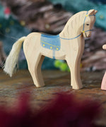 An Ostheimer white horse figure with blue coloured saddle placed on a wooden surface. These wooden figures are part of a wide range of expertly hand crafted wooden toys here at Babipur. 