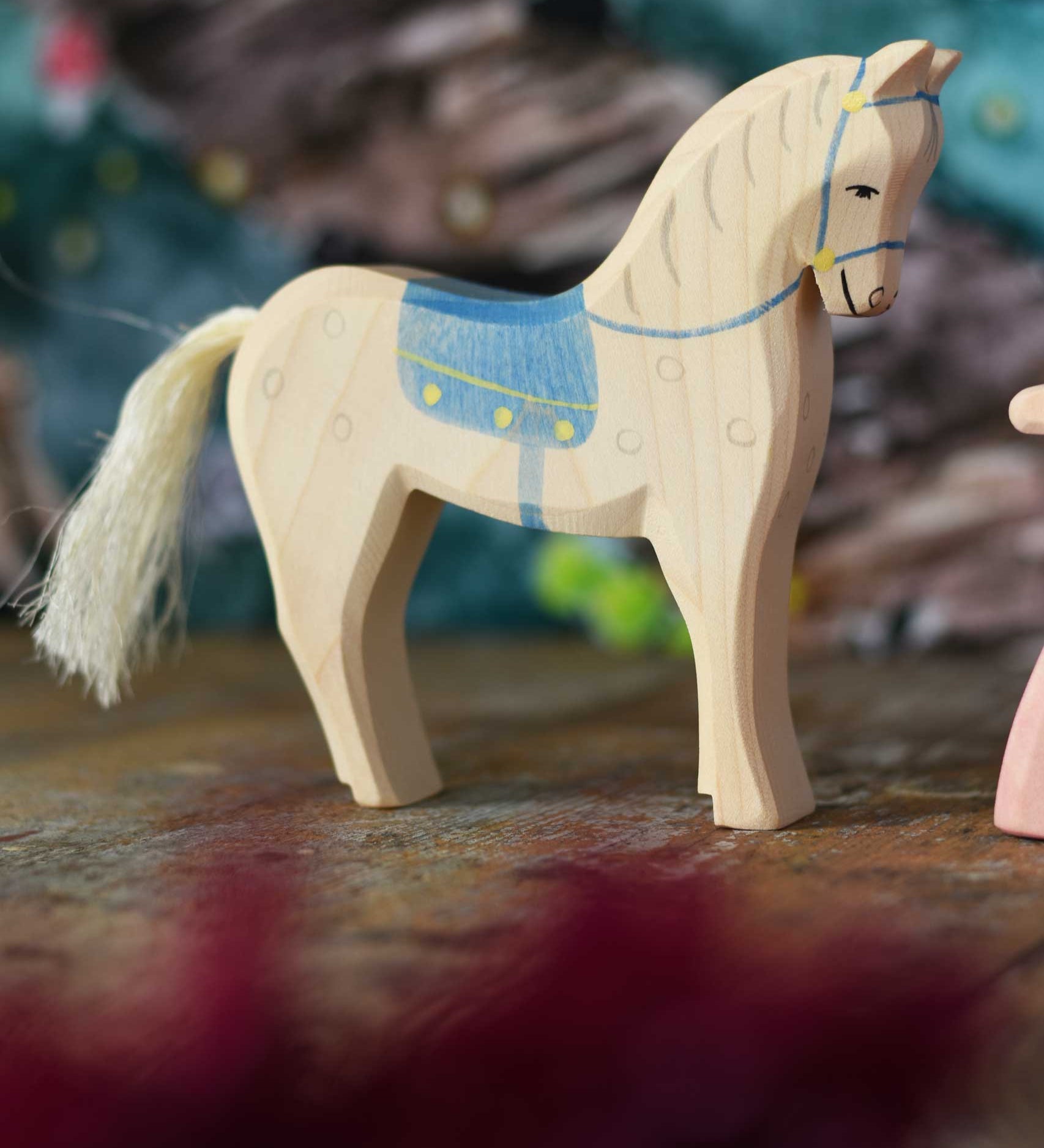 An Ostheimer white horse figure with blue coloured saddle placed on a wooden surface. These wooden figures are part of a wide range of expertly hand crafted wooden toys here at Babipur. 
