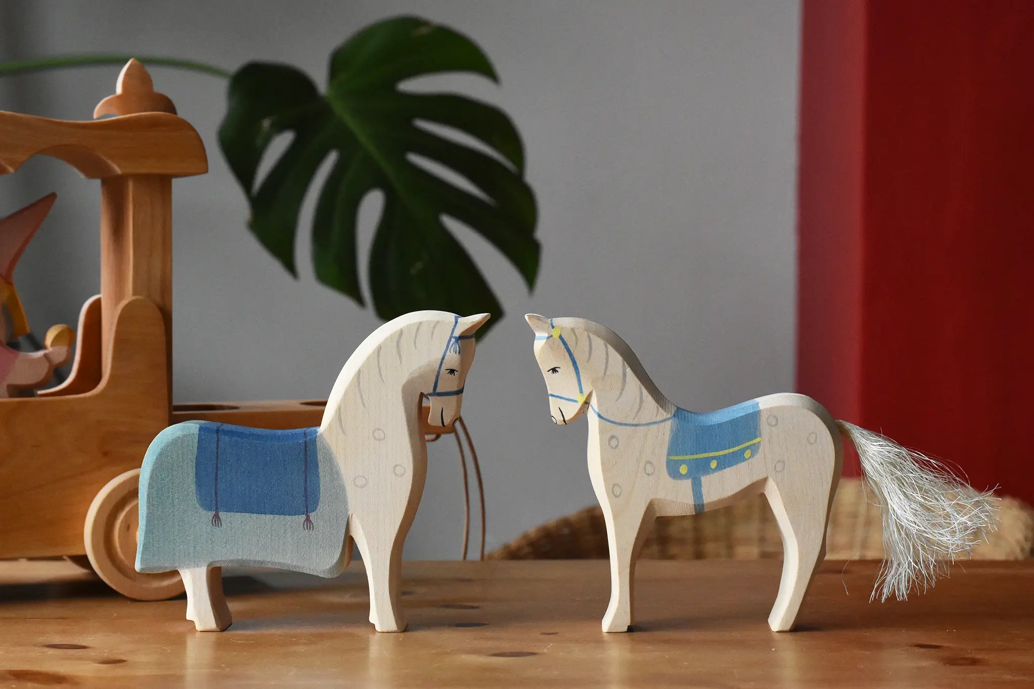 Two Ostheimer wooden white horse with blue saddle figures placed on a wooden surface with the coach house in the background.